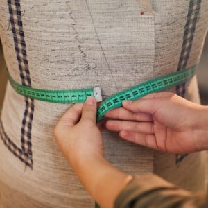 Close-up of tailor measuring the waist of mannequin with tape measure while sewing jacket in workshop